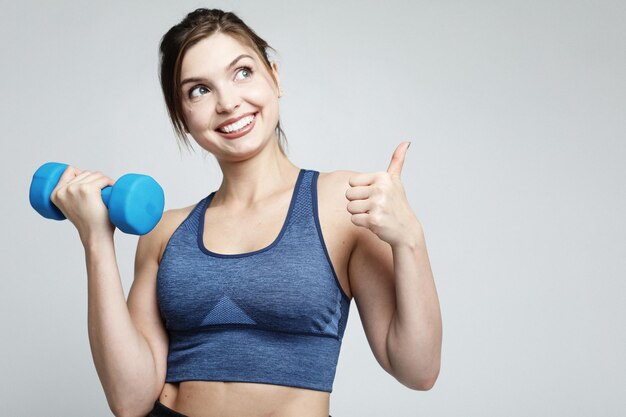 Photo d'une jeune femme en forme et en bonne santé souriante et tenant des haltères à l'épaule Sport et concept de personnes