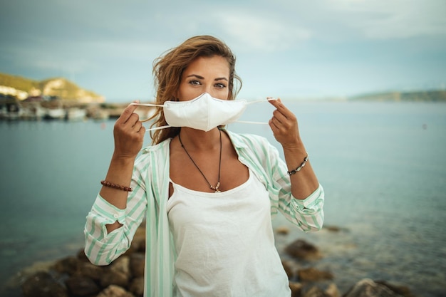 Photo d'une jeune femme heureuse avec un masque de protection N95 profitant de vacances sur la plage pendant le COVID-19.