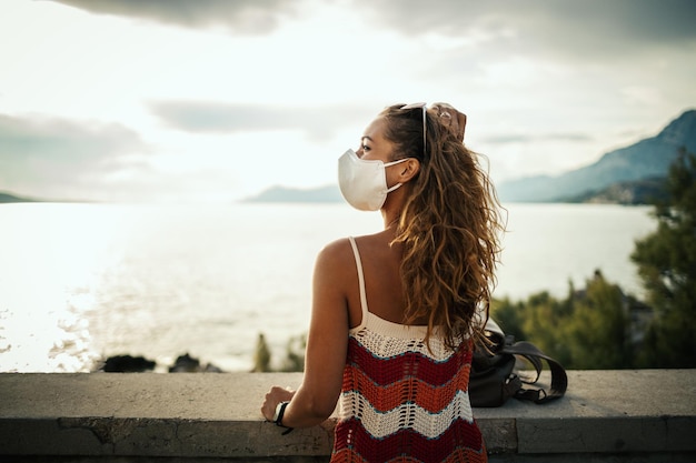 Photo d'une jeune femme heureuse avec un masque de protection passant du temps au bord de la mer lors de l'exploration d'une Méditerranée lors d'une pandémie de corona.