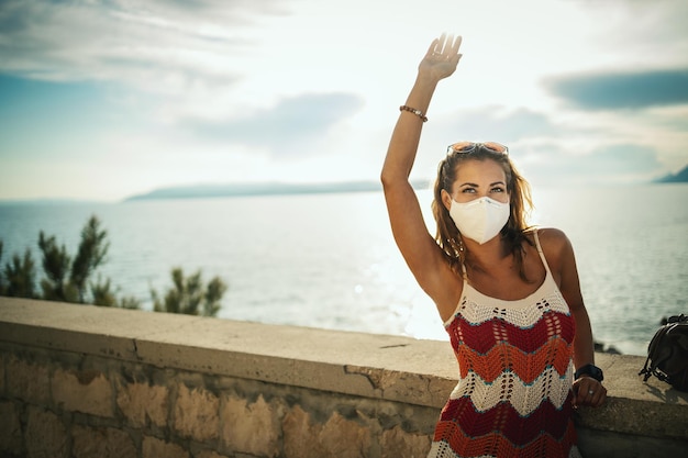 Photo d'une jeune femme heureuse avec un masque de protection passant du temps au bord de la mer lors de l'exploration d'une Méditerranée lors d'une pandémie de corona.