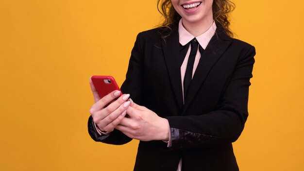 Photo de jeune femme heureuse posant isolée sur un mur jaune à l'aide d'un téléphone mobile.