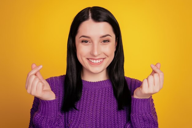 Photo d'une jeune femme joyeuse et positive souriante souriante montrant un geste d'argent isolé sur fond de couleur jaune