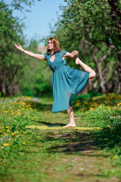 Photo de jeune femme en longue robe verte faisant du yoga en forêt le jour d'été.