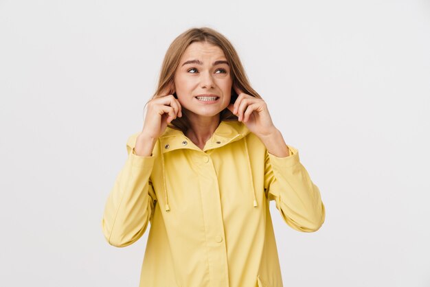 Photo d'une jeune femme malheureuse en imperméable se bouchant les oreilles et regardant de côté