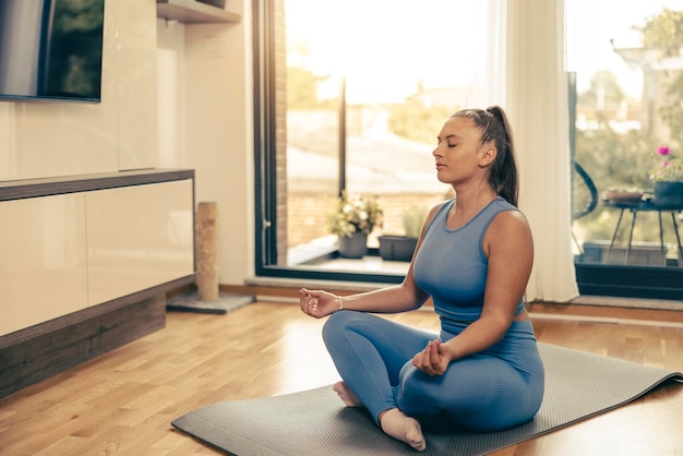 Photo d'une jeune femme mignonne méditant dans la position du lotus à la maison.