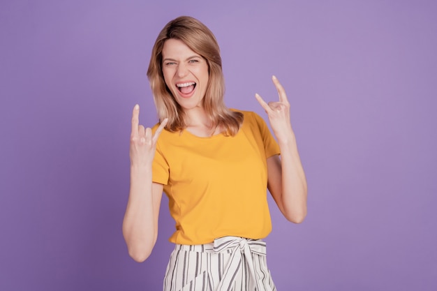 Photo de jeune femme montrant rock signe et crier s'amusant isolé sur fond de couleur violet