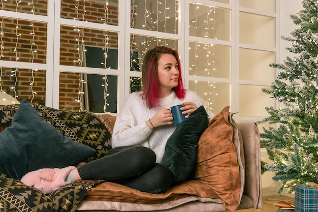 Photo d'une jeune femme rêveuse vêtue d'un pull tenant un cadeau de Noël souriant à l'intérieur de la chambre home house