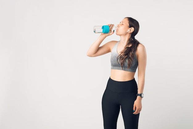 Photo de jeune femme s'hydratant sur un mur blanc