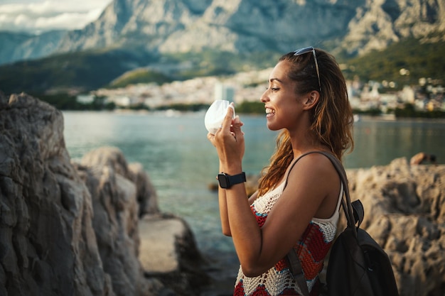 Photo d'une jeune femme souriante mettant un masque de protection et passant du temps au bord de la mer, explorant une Méditerranée à la pandémie de corona.