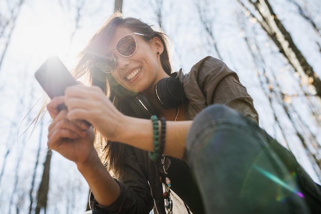 Photo d'une jeune femme souriante utilisant son smartphone tout en profitant de la nature.