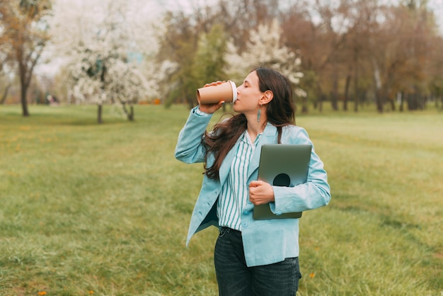 Photo de jeune femme en tenue décontractée dans le parc et buvant une tasse de café