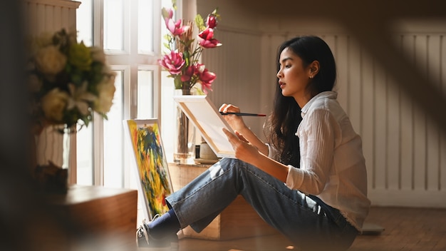 Photo de jeune fille artiste tenant un pinceau et dessinant des couleurs à l'huile sur toile