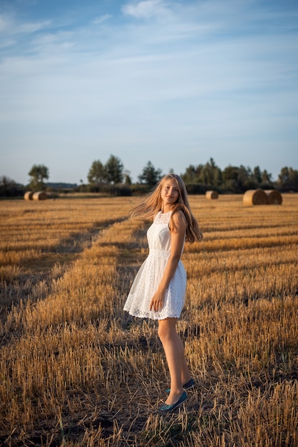 Photo d'une jeune fille blonde vêtue d'une robe blanche marchant dans le champ de seigle récolté