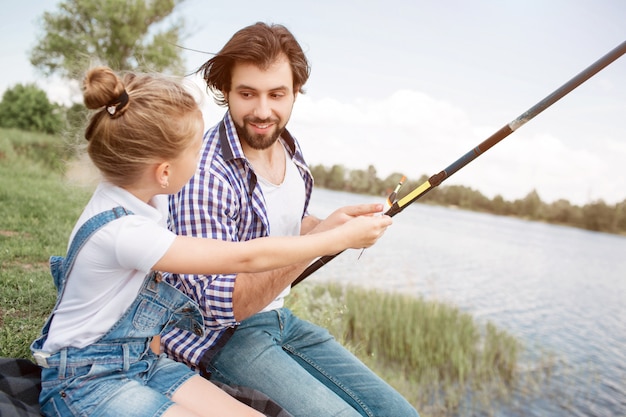 Une photo d'une jeune fille demandant à son père de pêcher un peu. Elle veut prendre la canne à poisson dans ses mains et le faire elle-même. Guy la regarde et lui donne une canne à poisson. Il aime sa fille.