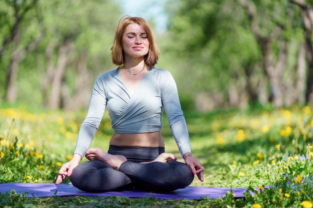 Photo de jeune fille faisant du yoga assis en position du lotus sur un tapis bleu dans les bois le jour d'été