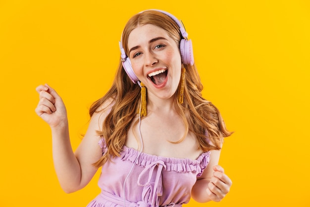 Photo d'une jeune fille heureuse souriante isolée sur un mur jaune écoutant de la musique avec des écouteurs.