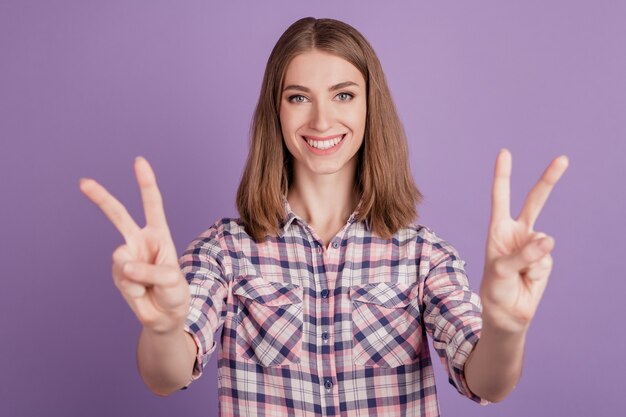 Photo de jeune fille joyeuse sourire positif heureux montrer la paix cool v-sign isolé sur fond de couleur violette