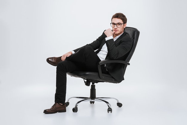 Photo de jeune homme d'affaires assis sur une chaise. Isolé sur mur blanc.