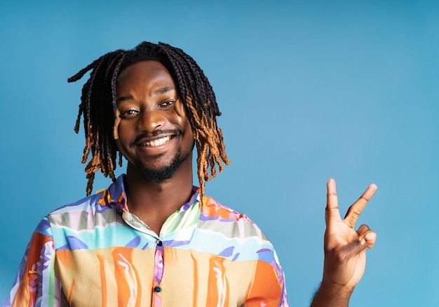 photo jeune homme africain heureux dreadlocks avec geste de paix portant une chemise de plage sur fond bleu