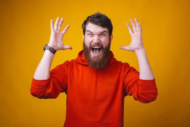 Photo d'un jeune homme barbu en colère criant à la caméra sur un espace jaune.