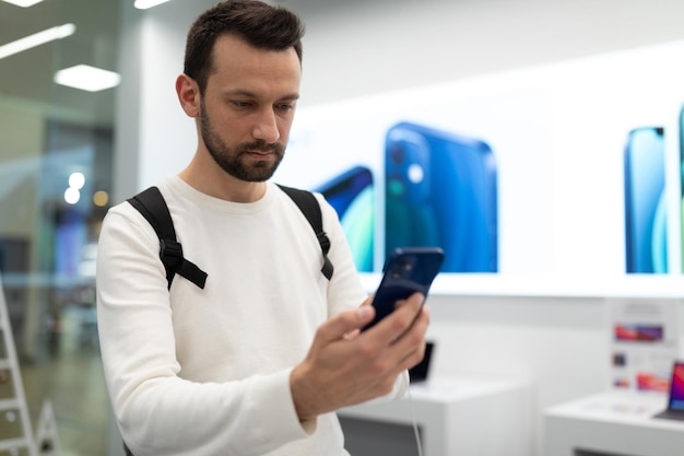 Photo d'un jeune homme brun pensant beau avec du chaume dans un sweat-shirt blanc choisit un mobile