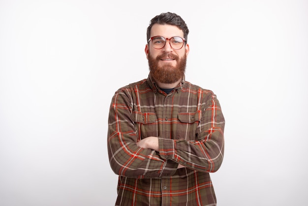 Photo de jeune homme en chemise debout sur un espace blanc avec les bras croisés et regardant confiant à la caméra