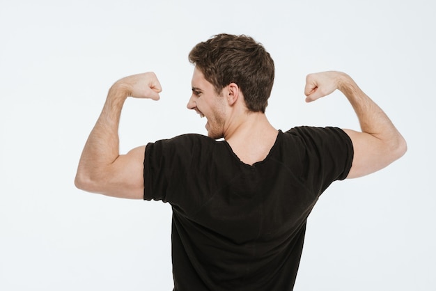 Photo d'un jeune homme criant vêtu d'un t-shirt noir debout sur fond blanc montrant ses biceps.