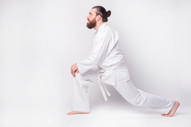 Photo de jeune homme en dobok faisant qui s'étend sur un mur blanc