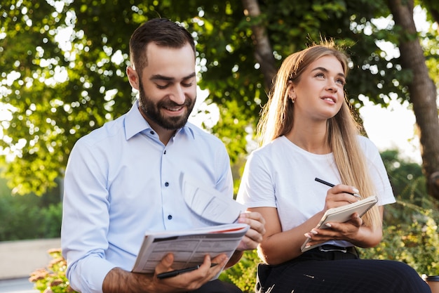 Photo d'un jeune homme et femme d'affaires concentré et heureux à l'extérieur dans un parc naturel, écrivant des notes dans des cahiers.