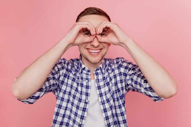Photo de jeune homme heureux sourire positif a donné de l'amusement grimace montrer les doigts signe ok jumelles oculaires isolées sur fond de couleur rose