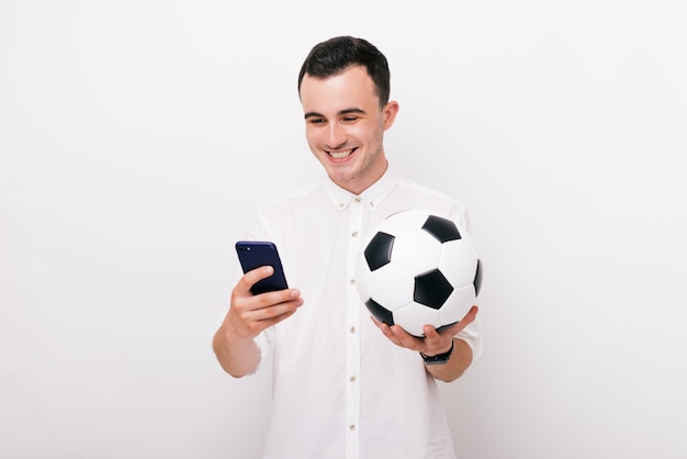 Photo de jeune homme heureux en tenue décontractée smartphone et ballon de football