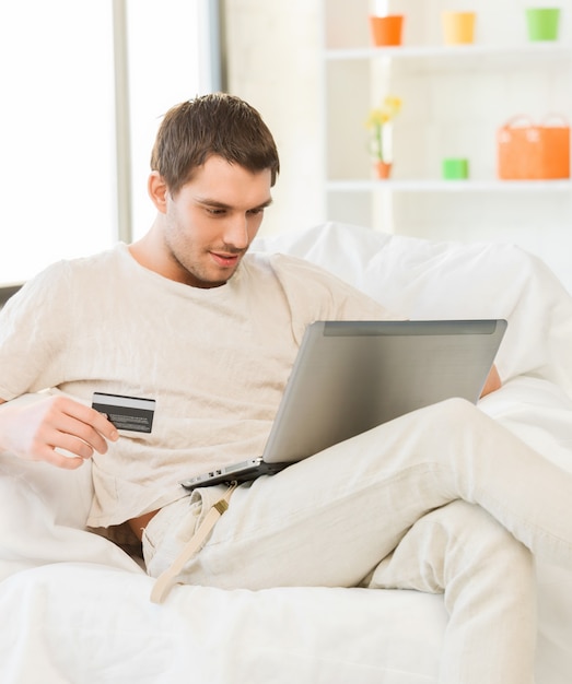 photo de jeune homme avec ordinateur portable et carte de crédit à la maison