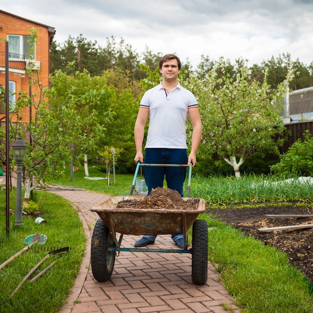 Photo de jeune homme portant une brouette de jardin