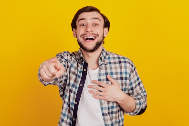 Photo d'un jeune homme se moquant de vous pointant vers la caméra et se moquant de vous ou se moquant de vous contre un mur jaune