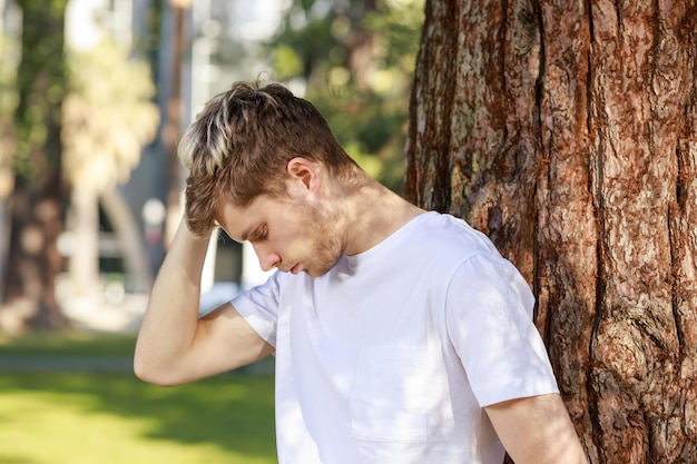 Photo d'un jeune homme se tenant au parc et s'appuyant sur l'arbre