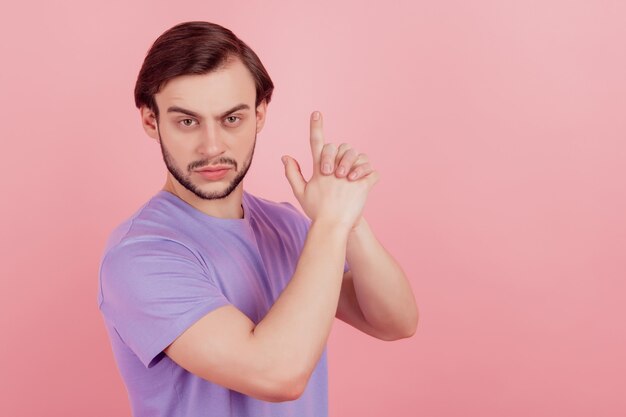 Photo de jeune homme séduisant sérieux montrer les doigts gun sign gangster sécurité dangereux isolé sur fond de couleur rose