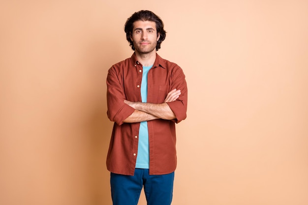 Photo d'un jeune homme sûr de lui, mains jointes, porter un t-shirt marron isolé sur fond de couleur beige