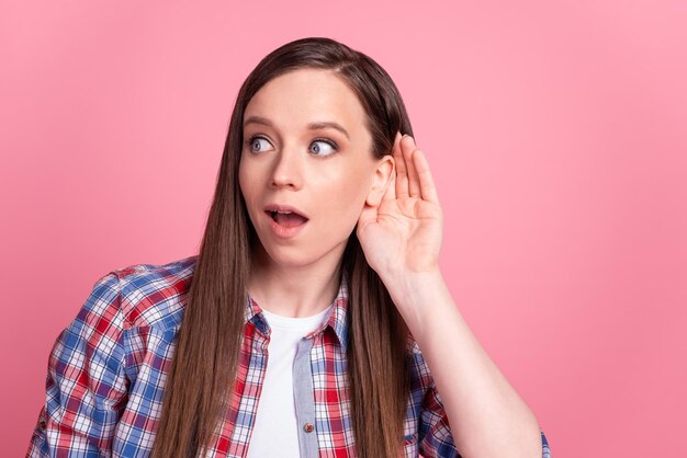 Photo de jeune jolie fille bras près des oreilles écouter la conversation des potins regarder l'espace vide isolé sur fond de couleur rose