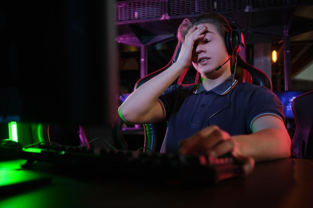 Photo d'un jeune joueur caucasien professionnel jouant en ligne sur son PC dans un club de jeux ou une cyber-arène. Il a l'air mécontent et contrarié. Le plan de match a mal tourné