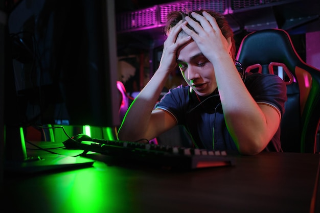 Photo d'un jeune joueur caucasien professionnel jouant en ligne sur son PC dans un club de jeux ou une cyber-arène. Il a l'air mécontent et contrarié. Le plan de match a mal tourné