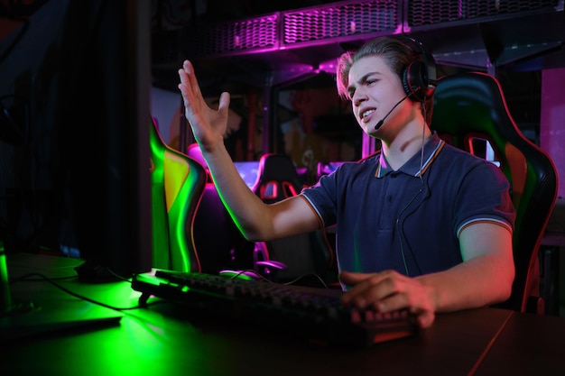 Photo d'un jeune joueur caucasien professionnel jouant en ligne sur son PC dans un club de jeux ou une cyber-arène. Il a l'air mécontent et contrarié. Le plan de match a mal tourné