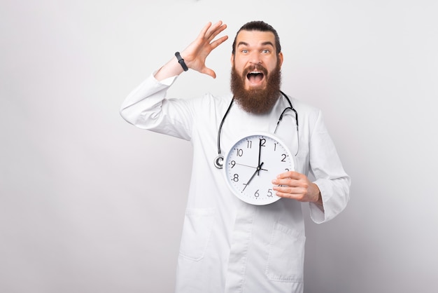 Photo d'un jeune médecin étonné tenant une horloge murale et faisant des gestes