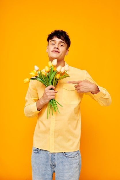 Photo de jeune petit ami romantique avec un bouquet de fleurs posant un cadeau fond jaune inchangé