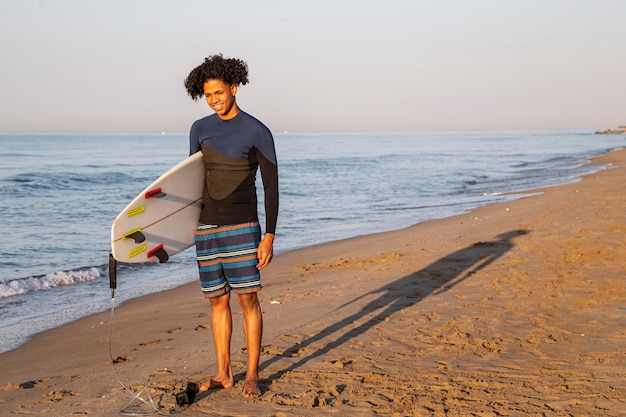 Photo d'un jeune surfeur souriant avec une planche de surf sur la plage.