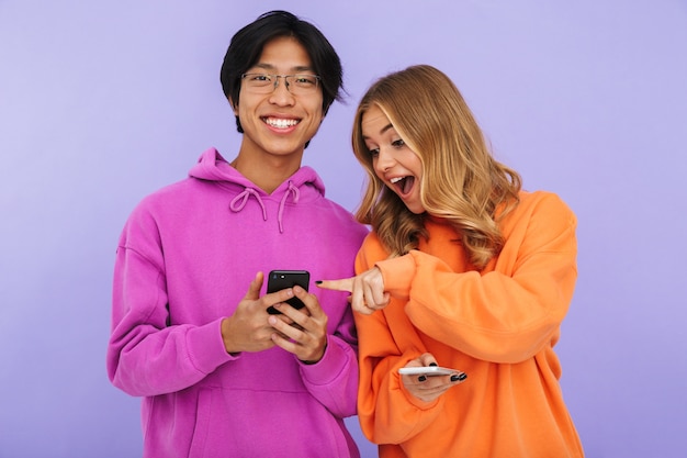 Photo de jeunes étudiants amis couple debout isolés, à l'aide de téléphones mobiles.