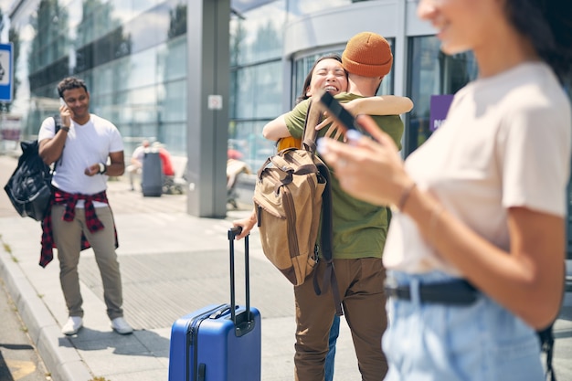 Photo De Jeunes Femmes Et Hommes Avec Une Valise étreignant à L'extérieur Où Des Amis Heureux De Se Voir