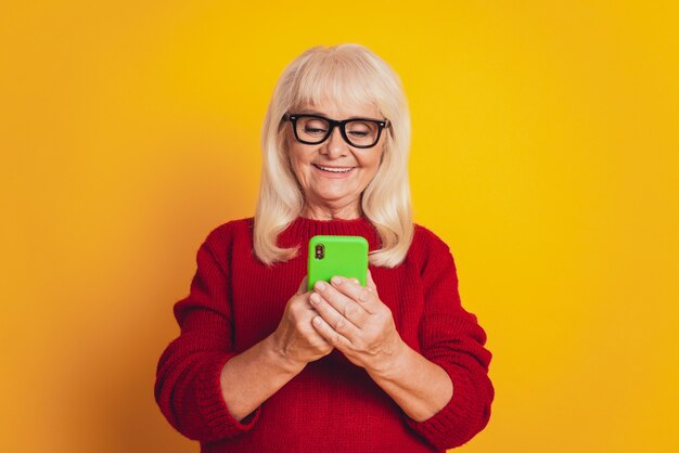 Photo de jolie dame senior porter des lunettes dispositif d'écriture isolé sur fond de couleur jaune