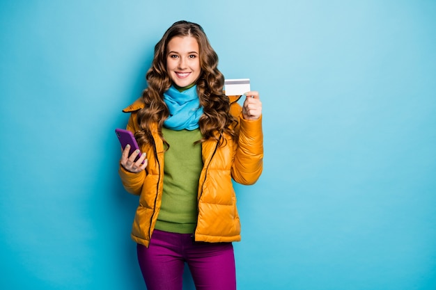 Photo de jolie dame tenir téléphone faisant des achats en ligne avec carte de crédit en plastique payer pass porter pardessus jaune écharpe pantalon violet cavalier vert mur de couleur bleu isolé