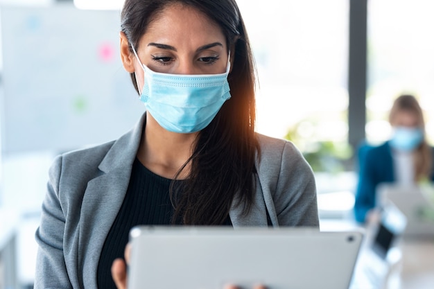 Photo d'une jolie femme d'affaires portant un masque hygiénique tout en travaillant avec sa tablette numérique dans l'espace de coworking.