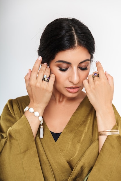 Photo d'une jolie femme indienne maquillée portant des bijoux ethniques et une robe en soie traditionnelle posant avec les mains isolées sur un mur blanc